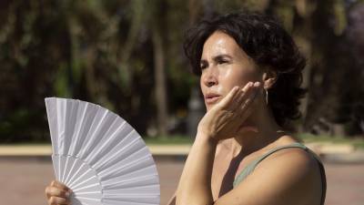 Mujer se da aire con un abanico en medio de la ola de calor | Fotografía de archivo