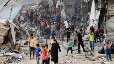 Los palestinos caminan entre los escombros de un edificio destruido y dañado en el centro de la ciudad de Khan Yunis, fuertemente bombardeado, en el sur de la Franja de Gaza, tras el bombardeo israelí nocturno, el 10 de octubre de 2023.