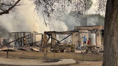 Varias personas regresan a las casas arrasadas por el fuego para retirar escombros.