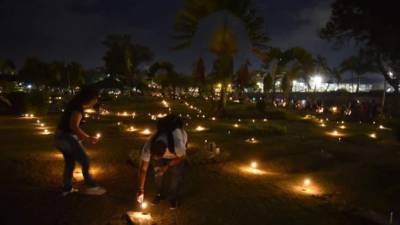 Varias personas prenden hoy velas junto a la tumba de un familiar en un cementerio durante la tradicional 'Noche de velitas' que se celebra en Cali (Colombia). EFE