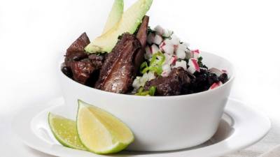 Sirva los frijoles con cerdo con cebolla morada picada, aguacate y limón.