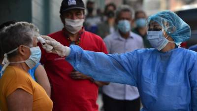 A nurse wearing protection measures the temperature of patients queuing to enter the Honduran Social Security Institute (IHSS) in Tegucigalpa on April 13, 2020. - 393 cases of COVID-19 and 25 deaths were reported in Honduras so far. (Photo by ORLANDO SIERRA / AFP)