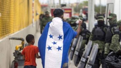 A boy and a man wrapped in an Hondura's national flag walk by a a cordon of military police outside a shelter for Central American migrants in Piedras Negras, Coahuila state, Mexico, near the US border, on February 8, 2019. - Around 1,700 migrants traveling by caravan reached the US-Mexican border Tuesday, just as President Donald Trump prepared to give a major speech certain to include calls for his long-sought wall. (Photo by Julio Cesar AGUILAR / AFP)