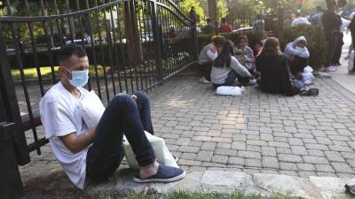 Migrantes venezolanos y mexicanos esperan en las afueras de la residencia de Harris tras ser dejados por un autobús en el que fueron enviados desde Texas.