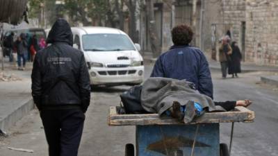 Dos personas cargan en una carreta el cuerpo de una mujer víctima del bombardeo.