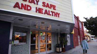 Un peatón pasa frente a una sala de cine cerrada, con el mensaje 'Mantente seguro y saludable' en la marquesina, el 19 de marzo de 2020 en Los Ángeles, California.