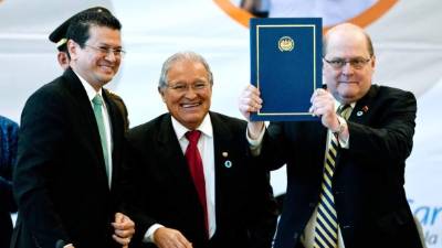 El presidente de Petrocaribe, Bernardo Álvarez (d), sostiene un documento entregado por el canciller salvadoreño, Hugo Martínez (i), acompañado por el presidente salvadoreño, Salvador Sánchez Cerén (c), durante la XIII reunión del Consejo Ministerial de Petrocaribe.