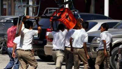 Estudiantes del Reyes caminan cargando pupitres en mal estado para usarlos en su aula de clases. Foto: Yoseph Amaya.