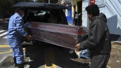 Empleados de una funeraria cargan el ataúd de una persona muerta por COVID-19. Fotos: AFP