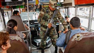 En la capital salvadoreña, un militar inspecciona si un pasajero de un autobús porta armas.