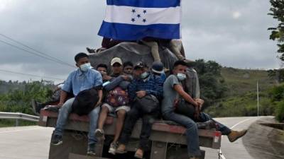 Migrants heading to the United States display an Honduran national flag as they hitchhike on the back of a truck near El Florido, in the Honduran department of Copan near the border with Guatemala, on January 15, 2021. - Hundreds of asylum seekers are forming new migrant caravans in Honduras, planning to walk thousands of kilometers through Central America to the United States via Guatemala and Mexico, in search of a better life under the new administration of President-elect Joe Biden. (Photo by Orlando SIERRA / AFP)