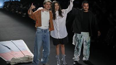 El baterista de la banda colombiana Morat, Martín Vargas (i), saluda al público presente al lado de dos de sus modelos luego de presentar prendas de la marca 'General' en una pasarela del Bogotá Fashion Week.