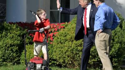 President Donald Trump high fives Frank Giaccio, 11, of Falls Church, Virginia, as he mows the lawn in the Rose Garden of the White House on September 15, 2017, in Washington, DC. Giaccio, who has his own lawn mowing business wrote a letter to the President asking if he could mow the lawn at the White House. / AFP PHOTO / Mike Theiler