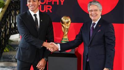 El presidente de Ecuador Guillermo Lasso (derecha) y el exjugador brasileño Lucio posan junto al trofeo de la Copa Mundo.