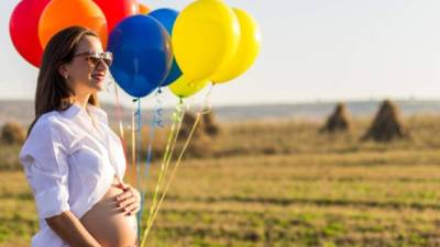 Beautiful pregnant woman with balloons on the field in susnet