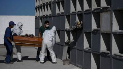 Cemetary workers wearing protective clothing place the coffin of a victim of the novel coronavirus, COVID-19, into a grave cubicle at Caju cemetary in Rio de Janeiro, Brazil, on May 9, 2020. - The novel coronavirus has killed at least 276,435 people worldwide since the outbreak first emerged in China last December, according to a tally from official sources compiled by AFP at 1900 GMT on Saturday. (Photo by Carl DE SOUZA / AFP)