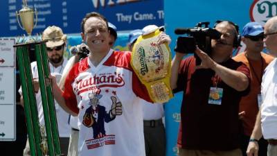 El competidor estadounidense levanta el trofeo y el cinturón tras vencer en el Concurso anual masculino de perritos calientes de Nathan's.// EFE/Peter Foley