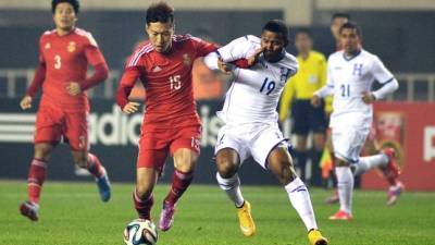 El jugador Wu Xi conduce el esférico ante la marca de Luis Garrido de Honduras.
