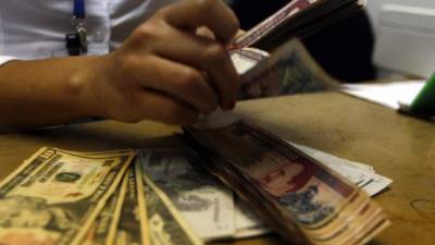 Una cajera de banco cuenta dólares y lempiras de diferente denominación. La liquidez de la banca es de L61,197.4 millones.