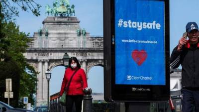 Una mujer con máscara facial camina cerca del parque Arches of Jubillee y frente a un mensaje de mantenerse a salvo en Bruselas, Bélgica, el 05 de mayo de 2020. Para contener la propagación del coronavirus, Bélgica está implementando pautas de confinamiento para el público que está programado para estará en vigor hasta el 11 de mayo de 2020. (Bélgica, Bruselas) EFE / EPA / OLIVIER HOSLET