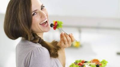 Smiling young woman eating fresh salad in modern kitchen