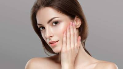 Young beautiful woman face portrait with healthy skin on gray background. Studio shot.