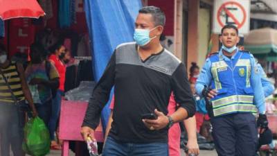Un hondureño civil usa su mascarilla, mientras que detrás hay un policía que no.