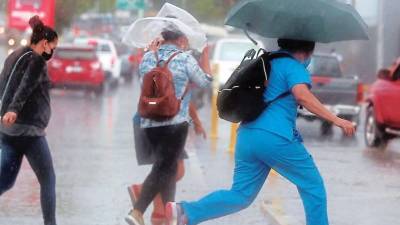 Hondureños corren por una calle mientras llueve sobre ellos | Fotografía de archivo