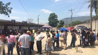 Con sombrillas, toallas y hasta con bolsas de plástico se protegen del sol las personas que esperan sus antecedentes.