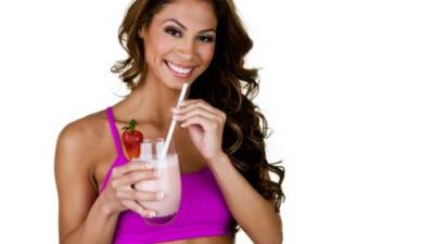 Horizontal composition of a woman wearing a sports bra and drinking a fruit smoothie shake