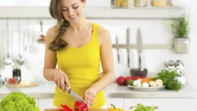 Happy young woman cutting fresh vegetables in kitchen