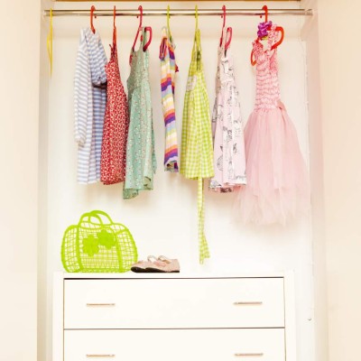square colour image of the interior of a little girl's wardrobe showing a row of dresses hanging on colourful coathangers and her handbag and shoes. Plenty of storage. Neatly organised.