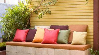 Aprovecha la pared de la casa, para confeccionar un sillón de madera y adornelo con colchonetas y cojines.