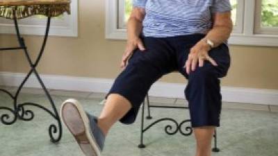 Senior Caucasian woman in late 70s raises her leg while performing physical therapy exercises at home to strengthen her legs