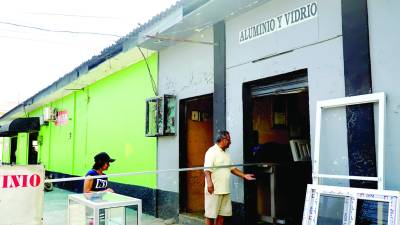 <b>Dos personas frente a un negocio que fabrica muebles y puertas de vidrio en San Pedro Sula.</b>