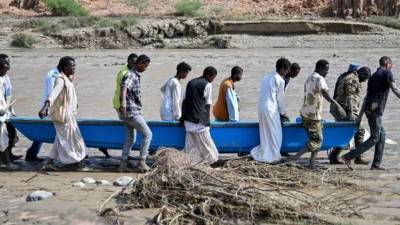 La gente lleva un bote en aguas fangosas después del colapso de la presa de Arbaat, a 40 km al norte de Puerto Sudán.