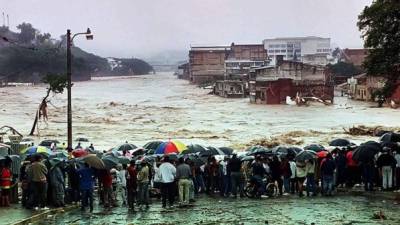 Decenas de hondureños observan cómo un río se desborda por las lluvias del huracán Mitch en 1998.