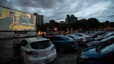 Varios vehículos y sus ocupantes durante la proyección de una película en un autocine.