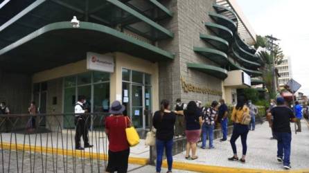 Varias personas hacen fila afuera de una agencia bancaria de San Pedro Sula.