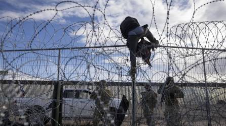 Un migrante escala una cerca para ingresar a EEUU frente a agentes de la Guardia Nacional de Texas.