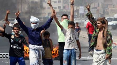 Jóvenes yemenitas vislumbran la V como señal de victoria cerca de la quema de neumáticos mientras los manifestantes protestan contra la inflación y el aumento de los costos de vida en la segunda ciudad de Adén.
