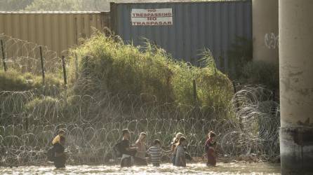 Algunos migrantes, vistos desde Piedras Negras, México, caminan a lo largo del río Bravo en busca de una abertura en la concertina en Eagle Pass, Texas, el 19 de julio de 2023.