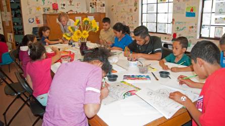 Un grupo de niños migrantes y algunos padres participando en una clase de arte del albergue para familias migrante en Tucson.