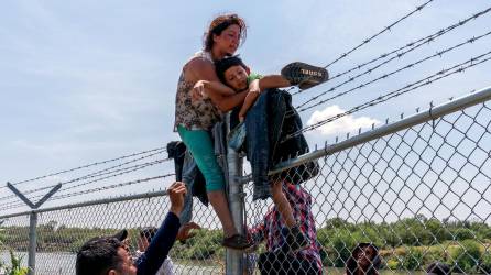 Migrantes saltan la barrera con alambre de púas instalada por las autoridades de Texas en la frontera.