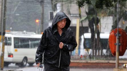 Hondureño se protege de la lluvia en Tegucigalpa utilizando una ‘chumpa’ mientras camina por una calle.