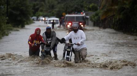 Personas cruzan con dificultad la carretera que se encuentra inundada producto de las intensas lluvias en San José de Ocoa (República Dominicana).