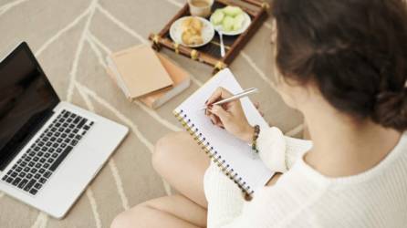 Female student sitting on the floor and making notes, view over the shoulder