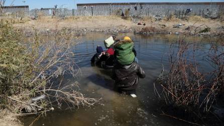Un grupo de migrantes cruza el río Bravo con varios niños.