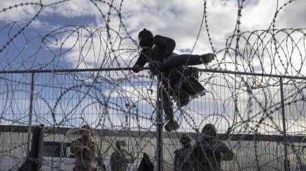 Un migrante escala la cerca alambrada para ingresar a EEUU frente a varios agentes de la Guardia Nacional de Texas.