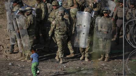 Una niña camina frente a integrantes de la Guardia Nacional de Texas, mientras vigilan la entrada de migrantes que permanecen en las inmediaciones del la frontera con Estados Unidos.